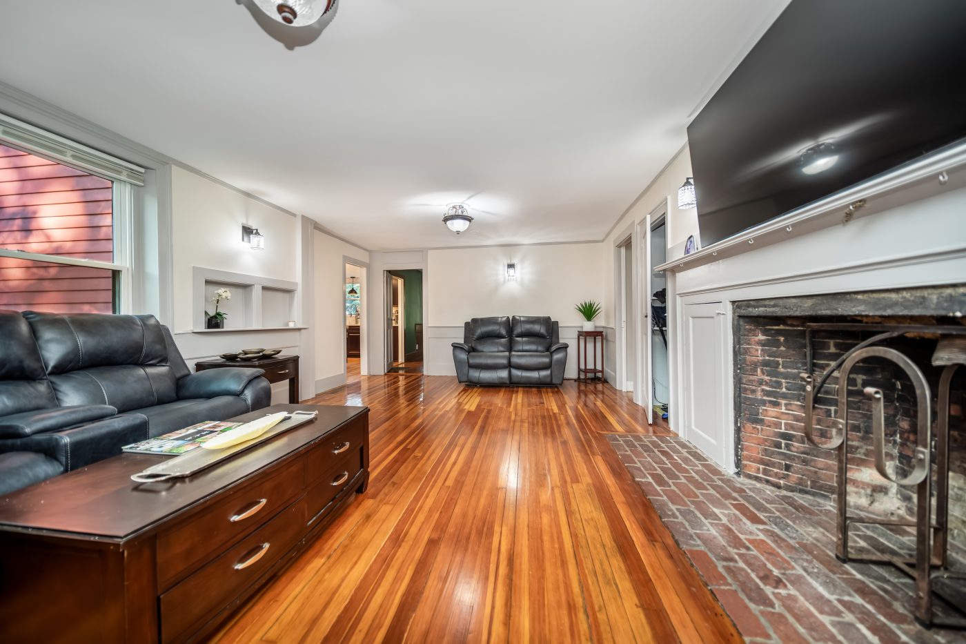 A room with a large brick fireplace and wide board floors