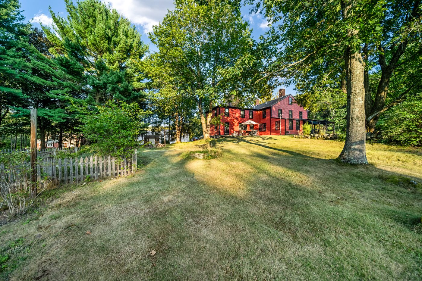 The house seen across the lawn beneath mature trees, behind a low fence